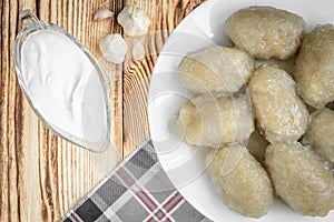 Potato dumplings with stuffed minced meat on a white plate and gravy boat with sour cream on wooden background