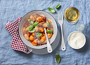 Potato gnocchi in tomato sauce with basil and parmesan and a glass of white wine on blue background, top view. Italian cuisine.