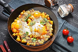 Potato hash with eggs and herbs for breakfast on black stone background