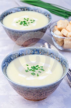Potato leek soup in blue ceramic bowl garnished with french cream and green onion, vertical