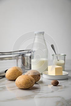 Potato, milk, salt, butter, nutmeg as ingredients with press and grinder for mashed potatoes on light marble background