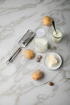 Potato, milk, salt, butter, nutmeg as ingredients with press and grinder for mashed potatoes on light marble background