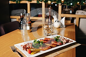 Potato pancakes with bacon on a white rectangular plate on a table in a restaurant. Table setting at the restaurant