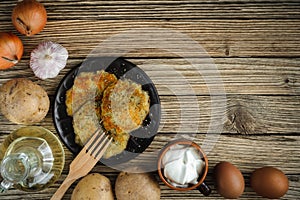 potato pancakes on a clay plate with a wooden fork with raw ingredients on a textured surface from old wooden planks. top view.