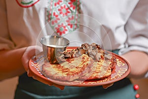 Potato pancakes dranik with sour cream, traditional Ukrainian dish. Waiter in traditional uniform serving dranyki.