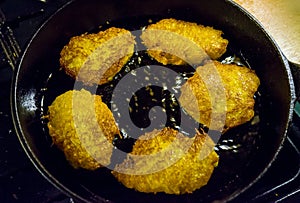 Potato pancakes, draniki, hash browns or fritters frying in old cast iron pan, skillet, selective focus