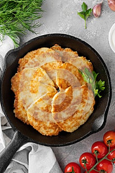 Potato pancakes, latkes or draniki with fresh herbs and sour cream in a cast iron pan on a gray concrete background. Top view,