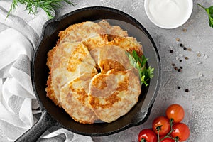Potato pancakes, latkes or draniki with fresh herbs and sour cream in a cast iron pan on a gray concrete background. Top view