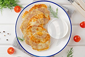 Potato pancakes, latkes or draniki with fresh herbs and sour cream on a plate on a white wooden background. Top view, copy space