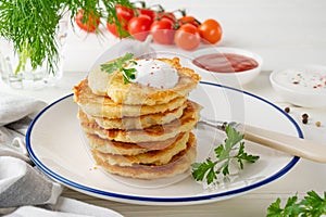 Potato pancakes, latkes or draniki with fresh herbs and sour cream on a plate on a white wooden background. Top view, copy space