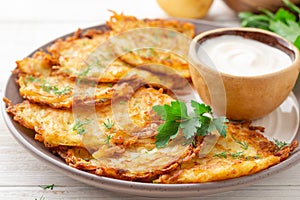 Potato pancakes or latkes or draniki with sour cream in plate on white wooden table