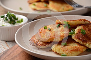 Potato pancakes or latkes or draniki with sour cream in plate on wooden table