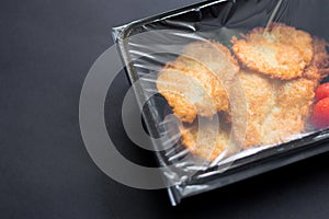 Potato pancakes in transparent sealed packaging on black background, top view. Food delivery in take away box