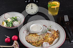 Potato pancakes on a white plate. Fresh vegetable salade and lemonade drink. Lunch time 12pm