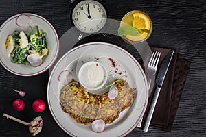 Potato pancakes on a white plate. Fresh vegetable salade and lemonade drink. Lunch time 12pm