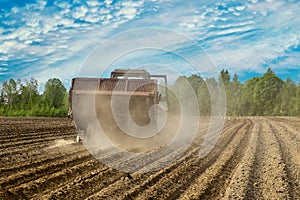 Potato planter in agricultural field raises cloud of dust in dry spring during sowing field work.