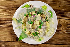 Potato salad with marinated mushrooms, eggs, red onion and mayonnaise on wooden table