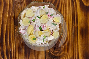 Potato salad with marinated mushrooms, sausage, onion and mayonnaise on wooden table