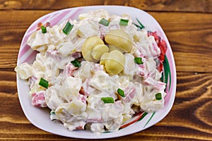 Potato salad with marinated mushrooms, sausage, onion and mayonnaise on wooden table