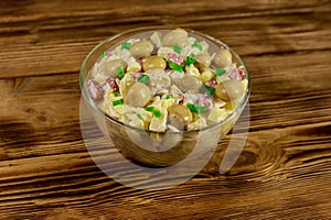 Potato salad with marinated mushrooms, sausage, onion and mayonnaise on wooden table