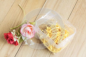 Potato stick in plastic bag and fake flower on wooden board