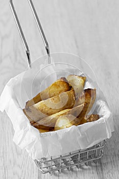 Potato wedges chips in a wire mesh serving basket with greaseproof paper.