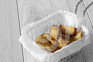 Potato wedges chips in a wire mesh serving basket with greaseproof paper.
