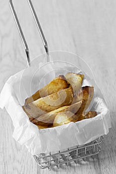 Potato wedges chips in a wire mesh serving basket with greaseproof paper. photo