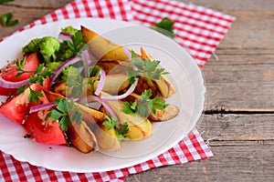 Potato wedges, cooked broccoli, fresh tomato slices with spices, red onion, green parsley leaves on a white plate