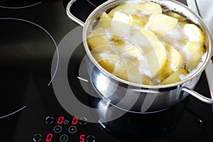 Potatoes boiling in small metal pan on the induction stove in the kitchen