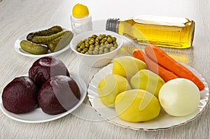 Potatoes and carrots, beetroot, onion, green peas, gherkins, salt shaker, bottle of vegetable oil for vinaigrette on table
