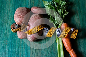 Potatoes, celery and carrots and a tailor& x27;s inch. Close-up on green wooden background. Christmas binge post diet concept