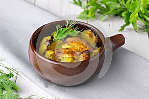 Potatoes, chicken and zucchini baked in a clay pot on a light background