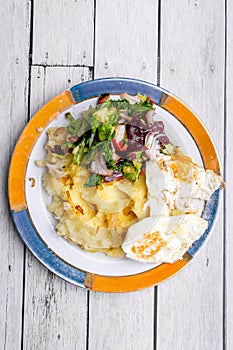 Potatoes, fried eggs and salad as a dinner. White wooden background. From above