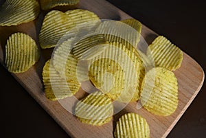 Potatoes fried wavy, embossed, potato chips with sour cream and greens, facies on a wooden board