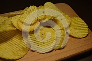 Potatoes fried wavy, embossed, potato chips with sour cream and greens, facies on a wooden board