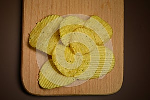 Potatoes fried wavy, embossed, potato chips with sour cream and greens, facies on a wooden board