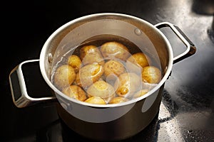 Potatoes with peel in a stainless steel pot with boiling water on the stove, healthy cooking concept, copy space, selected focus