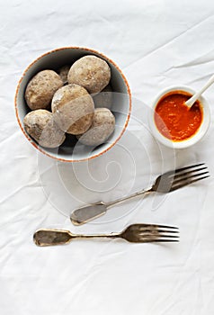 Potatoes in a white bowl with red sauce and wok on a white tablecloth. A traditional Canarian dish is papas arrugadas.