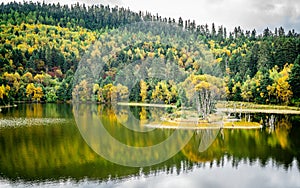 Potatso national park view with Shudu lake with islet and forest with autumn colours and water reflection Shangri-La Yunnan China