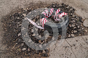 Pothole in asphalt road covered with tire cover wrapped in red and white safety strip.