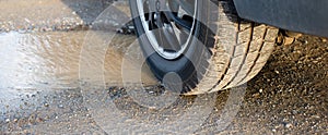 Pothole in the road, car wheel besides the puddle, water hole after rain, conditions of streets in Germany, damaged highway