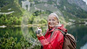 Potrait of active senior woman on hike in autumn mountains taking photos with camera.