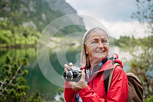 Potrait of active senior woman on hike in autumn mountains taking photos with camera.