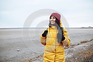 Potrait of a young woman tourist with a backpack walking on sideroad among vast empty winter valley lowland. Female traveller