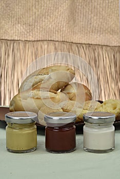 Pots with mayonnaise and ketchup with paes in the background