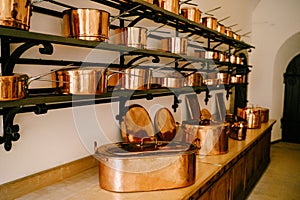 Pots and saucepans in gold-colored copper in various sizes on shelves in a room with a long wooden table