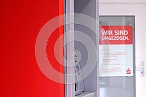 Potsdam, Germany - February 17, 2024: bright red wall, seeing part of grey ATM machine and blurred poster on door with