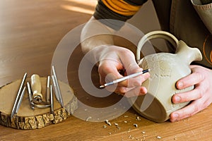 Potter carving ornament on jug. Master working in Pottery studio with equipment Wooden Modeling Tools