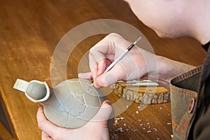 Potter carving ornament on jug. Master working in Pottery studio with equipment Wooden Modeling Tools